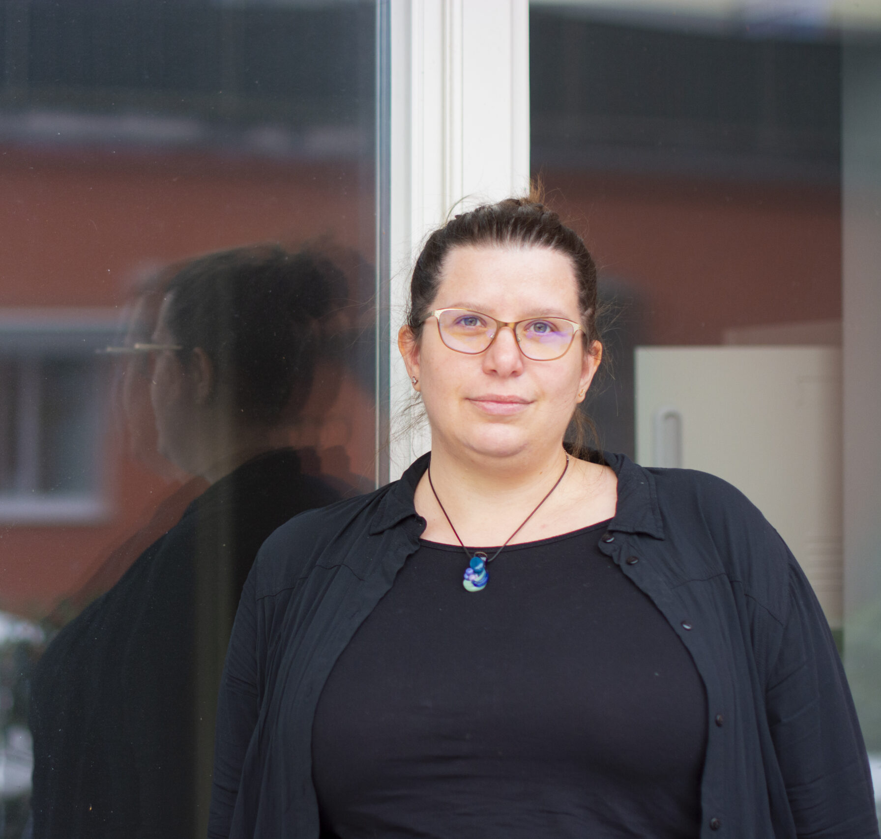 Porträttfoto av Johanna Lindblad som driver JL Resonans. Hon ler varmt mot kameran. Hon har en trygg och lugn utstrålning och står lutad mot ett fönster.